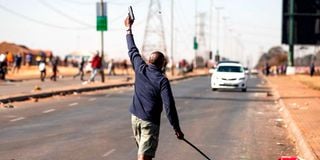 A man fires a hand gun in the air to disperse a mob of alleged looters outside of the Chris Hani Mall