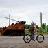 A woman rides bicycle past remains of Russian APC 