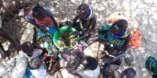 A woman and children eat wild leaves in Kanamkuny village in Turkana County 