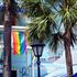 A balcony in Key West, Florida, displays a gay pride flag, with palm trees and a street lamp