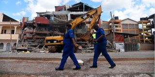 Police officers walking past the debris of a five-storey building that collapsed in Ruiru