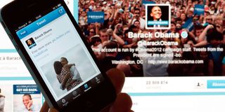 A person poses with a cell phone in front of a computer screen to check Barack Obama's tweet 