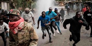 Protesters run away from water released by a police’s water cannon vehicle during a mass rally in Kibera