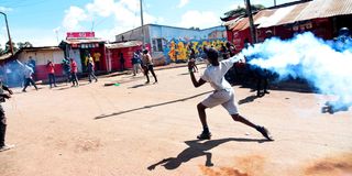 A protester throws a teargas canister back at anti-riot police in Kibra, Nairobi