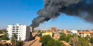 A column of smoke rises behind buildings near the airport area in Khartoum