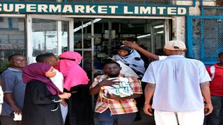 A man walks with packets of subsidised maize flour as members of the public queue outside a supermarket in Mombasa