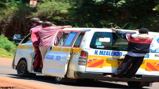 Four men precariously hang on a moving matatu