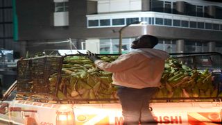 A loader hangs onto a vehicle at Marikiti market