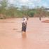 A woman with a child wades through a flooded Bura-Garisa highway.